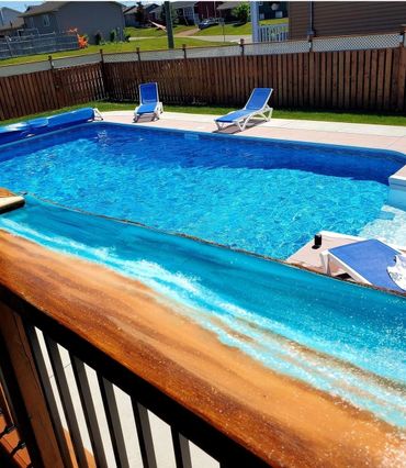 Backyard pool surrounded with lounge chairs, seen from deck with ocean color edge