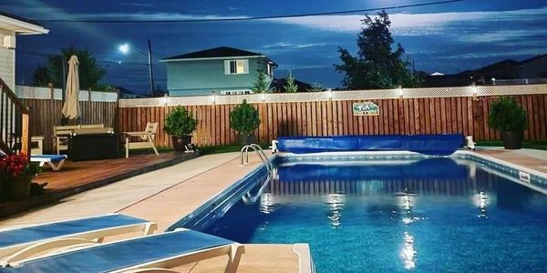 Night sky and moon overlooking backyard inground pool with lounge chairs alongside.