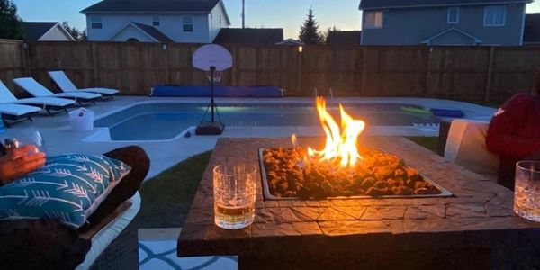 Fireplace with drink glass on table, with inground pool and fence in background