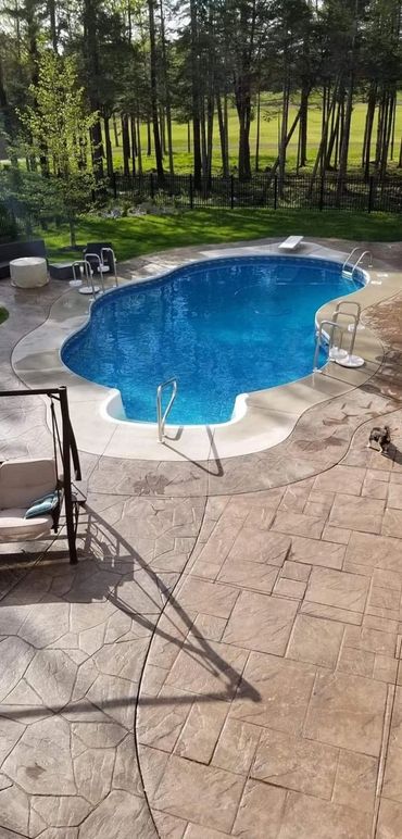 Inground swimming pool with concrete walkway and landscaping in background