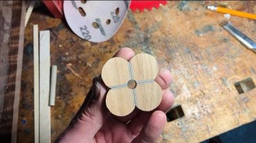 Hand holding a wooden flower-shaped piece with a central hole and grooves.