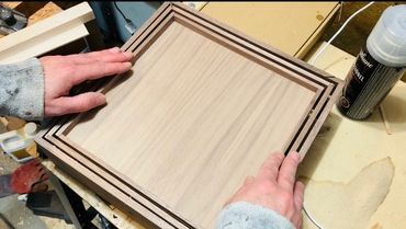 Hands holding a wooden frame with layered grooves on a workbench.