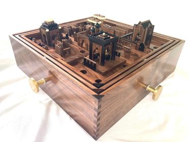 Intricately carved wooden box with miniature architectural structures and brass knobs.