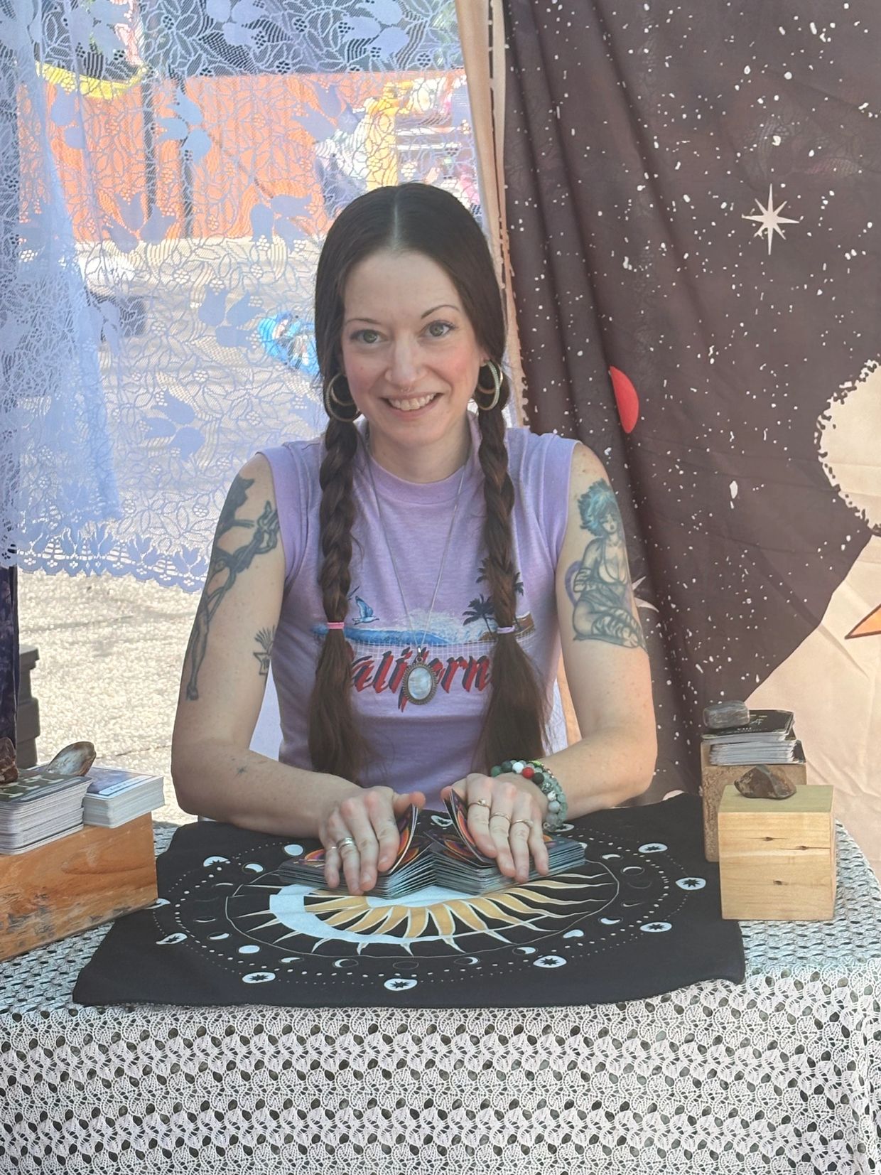 Smiling woman with braided hair shuffles tarot cards on a decorated table.