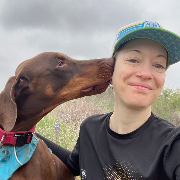 A Doberman dog gently nuzzles a person's face outdoors.