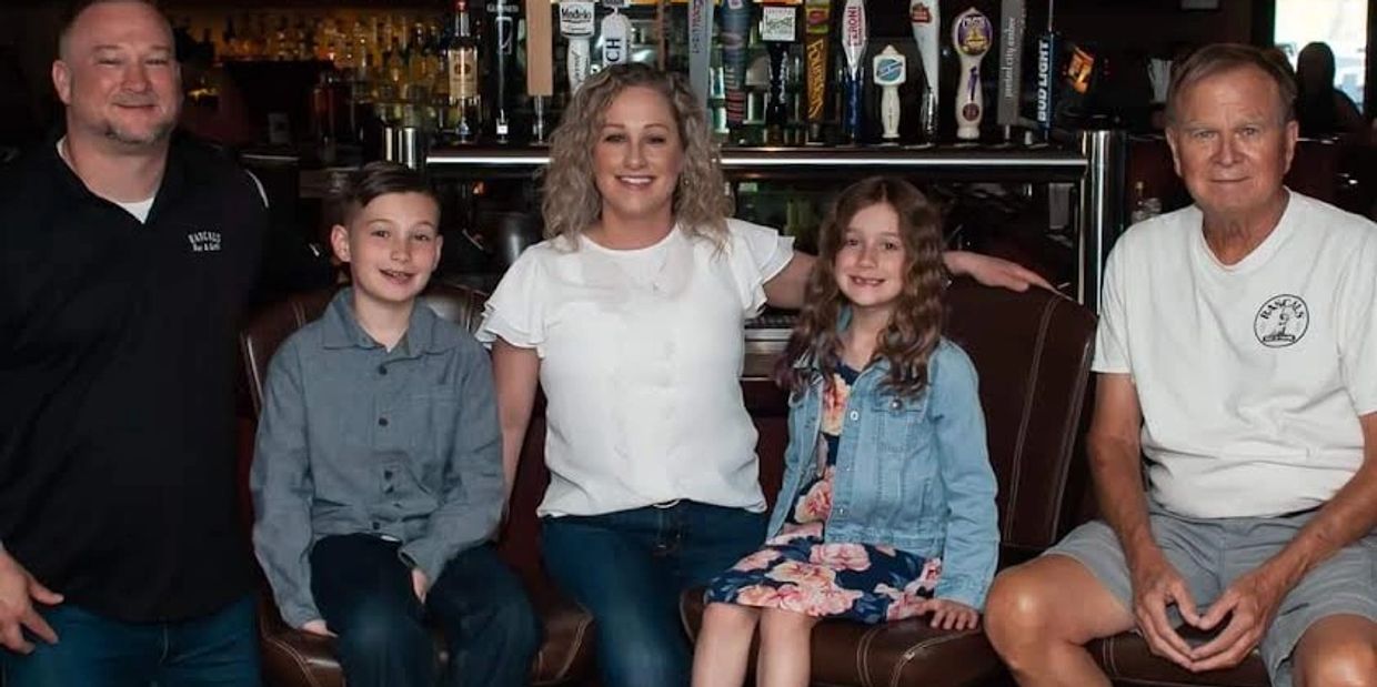 A family of five sitting on bar stools in a cozy bar setting, smiling at the camera.