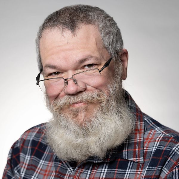 Smiling elderly man with glasses and a beard.