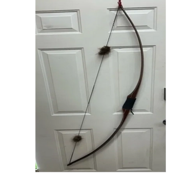 Traditional wooden recurve bow hanging on a white door.