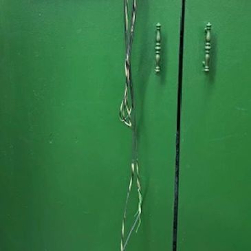 Green cabinet with custom archery logos and a hanging twisted metal tool.