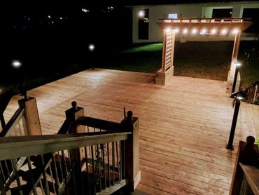 Wooden deck with pergola and string lights at night.