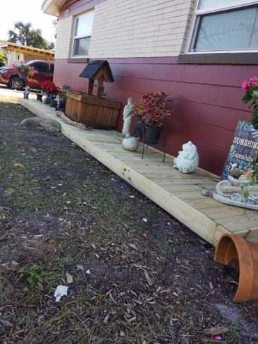 Decorative garden area with plants and statues on a wooden platform beside a house.