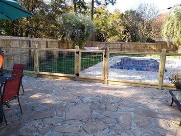 Backyard patio with stone flooring, fenced pool, and palm trees in the background.