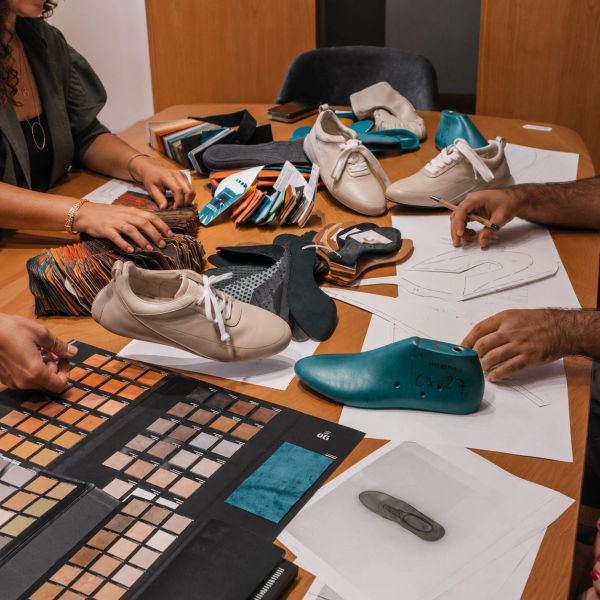 Designers working on shoe prototypes and material samples at a table.