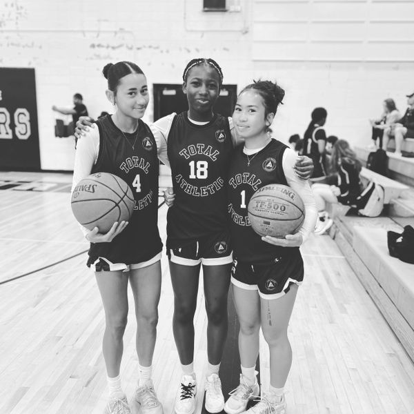 Three young female basketball players pose together on the court, smiling.