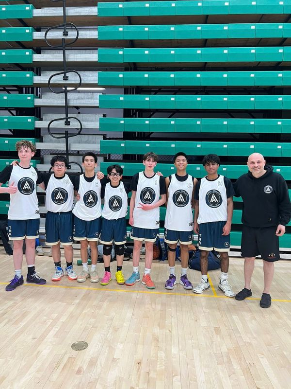 A youth basketball team posing with their coach in a gymnasium.