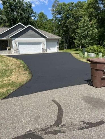 Freshly paved black driveway leading to a suburban home with a three-car garage.