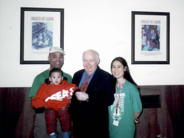 Four people posing indoors with framed pictures behind.