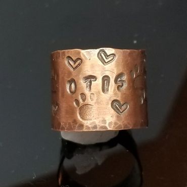 Copper ring with paw prints, hearts, and the word "OTIS" engraved.
