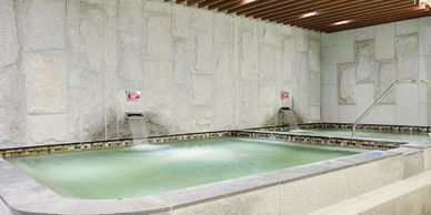Luxuriously large spa baths with premium grey tiles, wooden slat ceiling, & water flowing feature