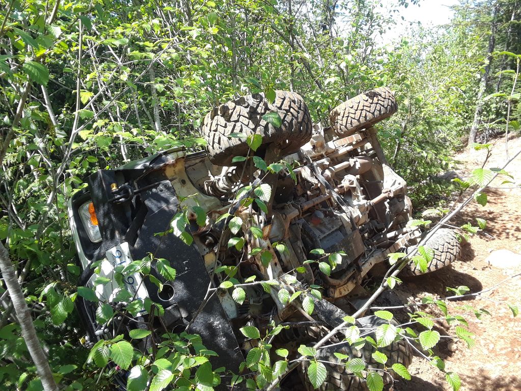 Off-road vehicle flipped upside down in dense forest foliage.