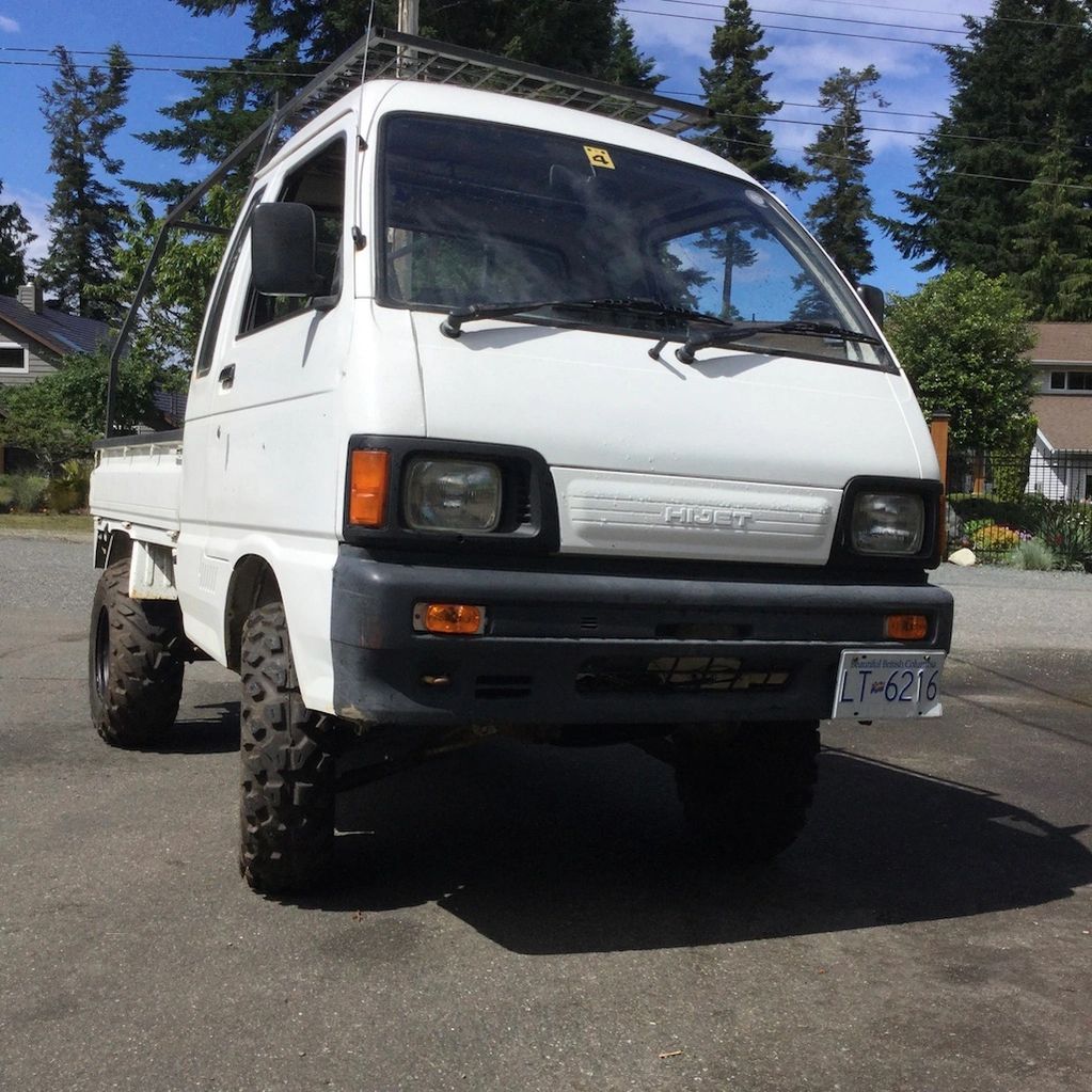 White Daihatsu Hijet mini truck with off-road tires parked outdoors.