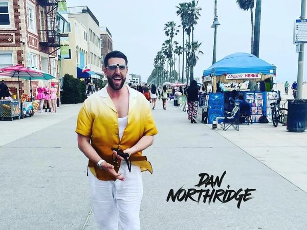 A man in a yellow and white shirt walking joyfully on a busy palm-lined street.