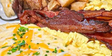 A hearty breakfast with bacon, scrambled eggs, hash browns, and cheese-covered eggs.