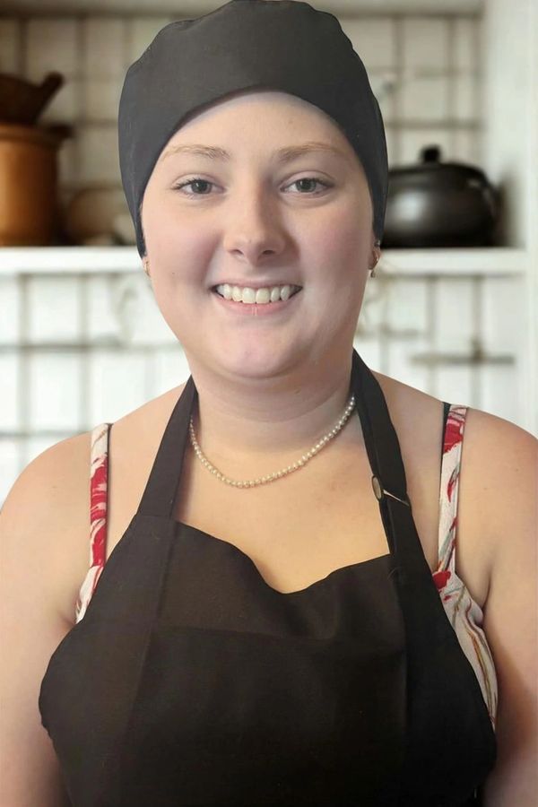 Smiling woman in kitchen wearing black apron and headscarf.
