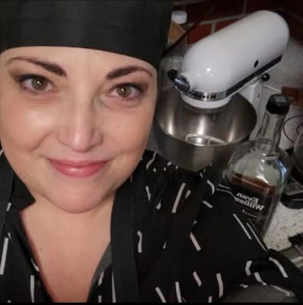 Smiling chef in black attire in a kitchen.