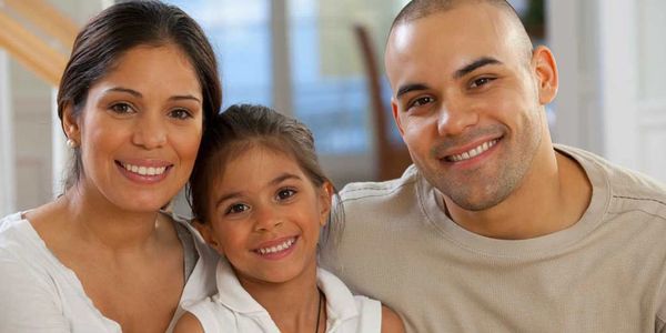 A happy family of three smiling together indoors.