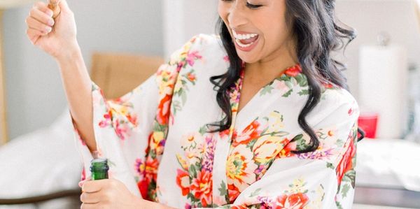 Happy and ecstatic bride opening bottle of champagne. Hair is down, curled with soft natural makeup