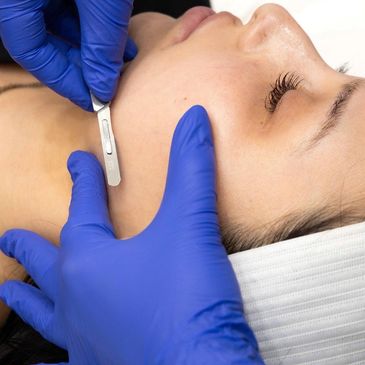 Close-up of a facial shaving treatment with a straight razor and blue gloves.