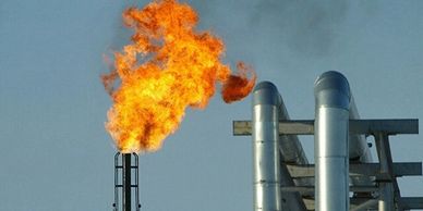 Flame burning from an industrial gas flare stack against a clear sky.