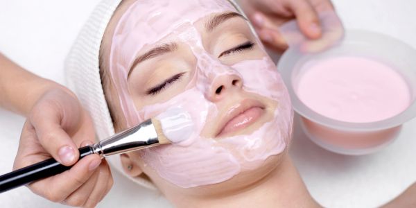 Woman getting a pink facial mask applied.