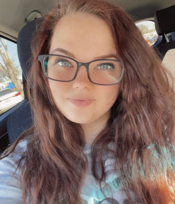 Young woman with long red hair and glasses smiling in a car.