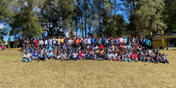 Large group photo outdoors on a sunny day with trees in the background.