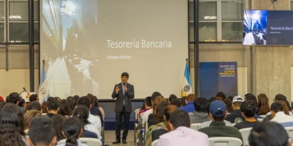 A speaker presents on banking treasury to an attentive audience in a conference room.