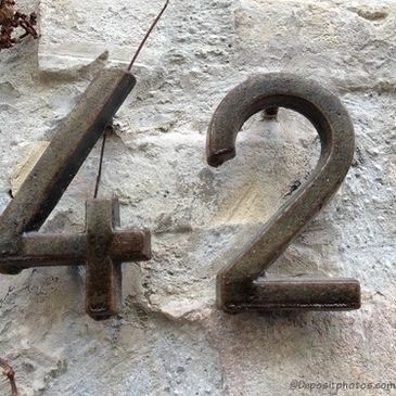 Rusty metal numbers 4 and 2 on a textured stone wall.