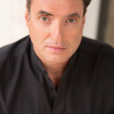 Close-up portrait of a man with light skin and dark hair wearing a black shirt.