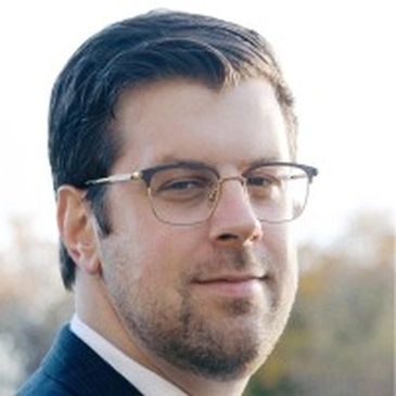 Portrait of a man wearing glasses and a suit outdoors.