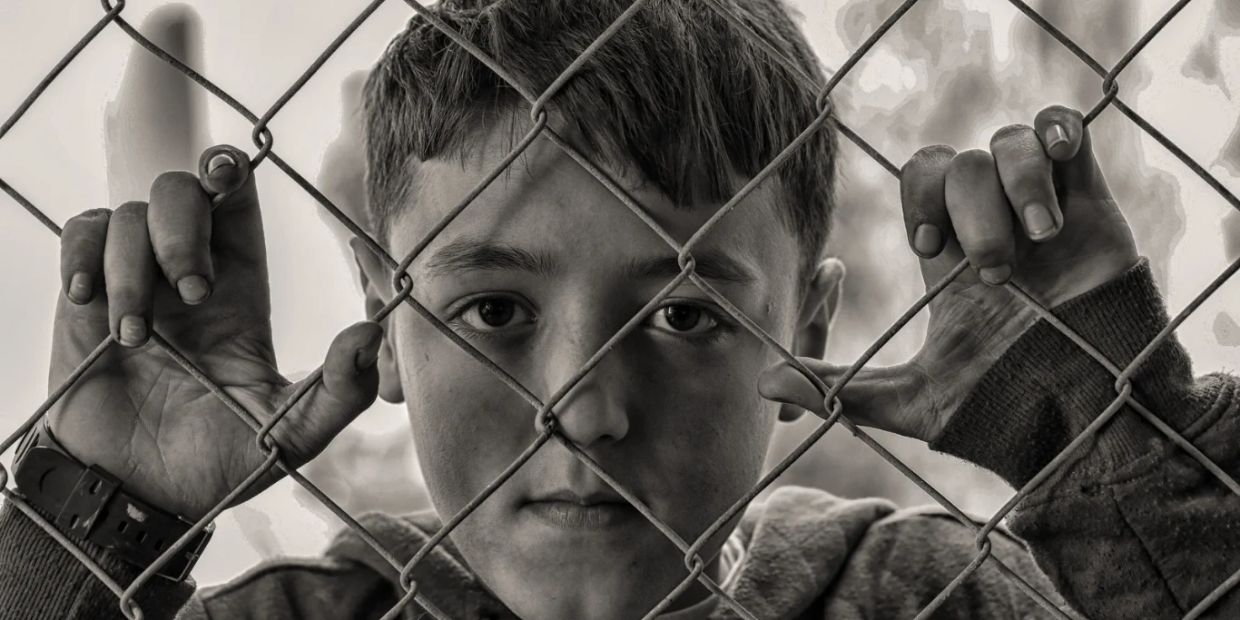 Boy looking through a chain-link fence.