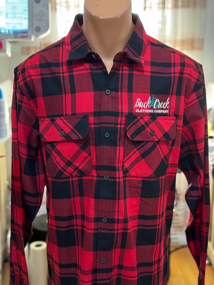 Red and black plaid shirt with buttoned pockets and logo on chest.