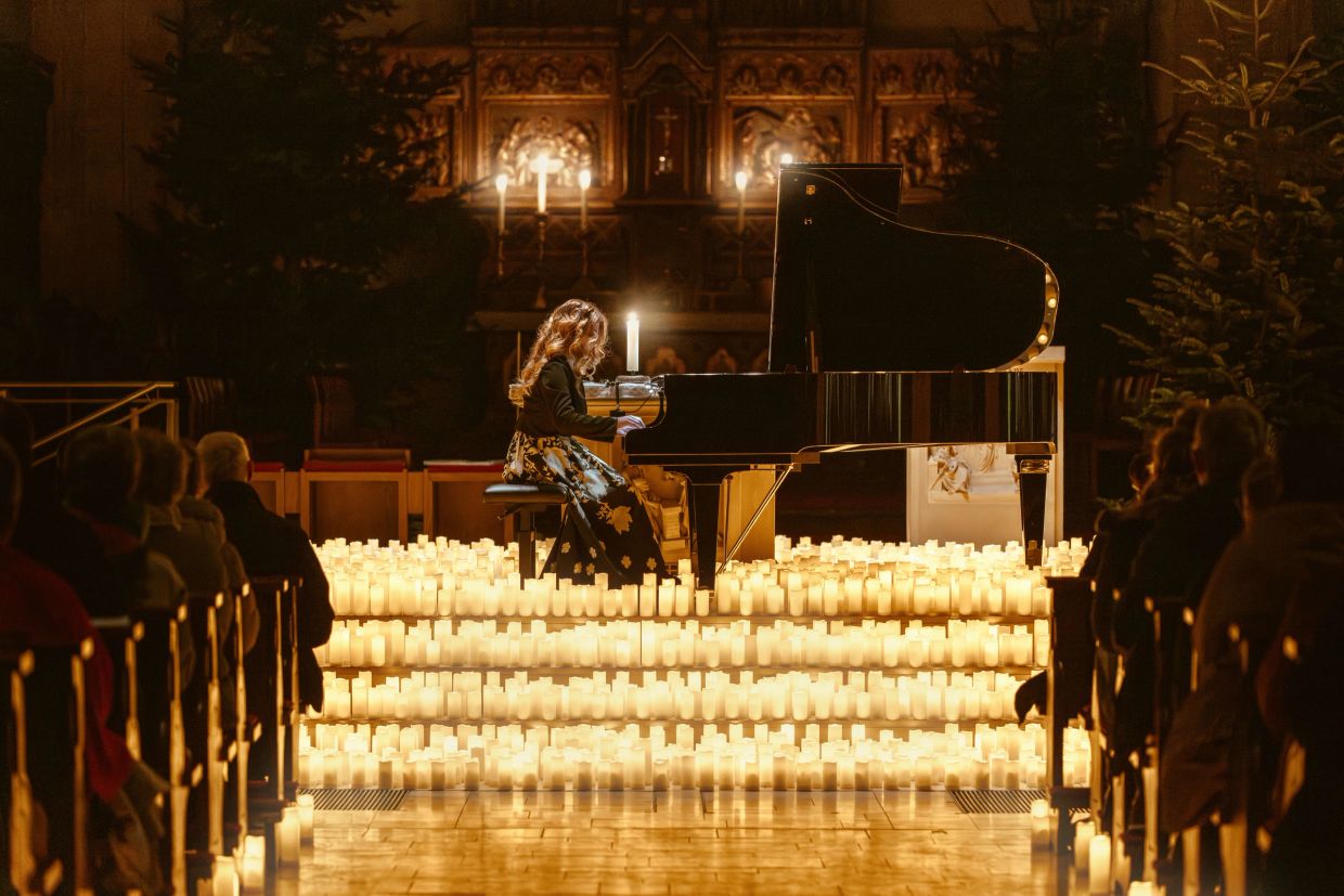 Ein Mädchen spielt Klavier, umgeben von Kerzenlicht in einer Kirche.