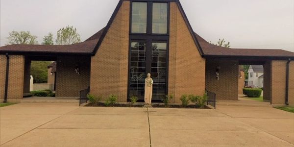 Brick church building with a statue in front and large stained glass windows.