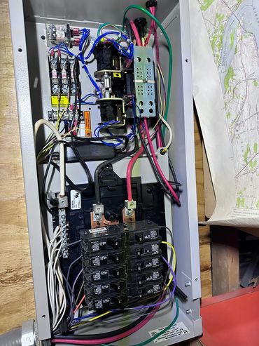 Open electrical panel with circuit breakers and wiring inside a metal enclosure.