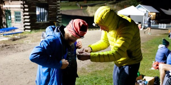 Two people outdoors at night adjusting clothing.