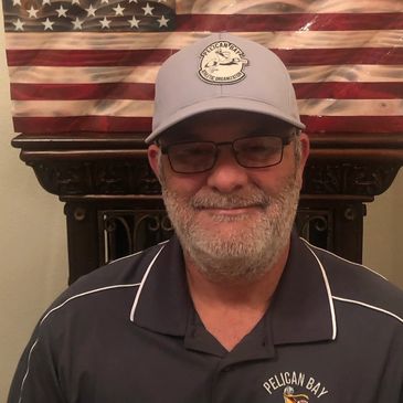 Smiling man in Pelican Bay cap and shirt with American flag background.