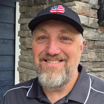 Smiling man with a beard wearing a hat with an American flag design.