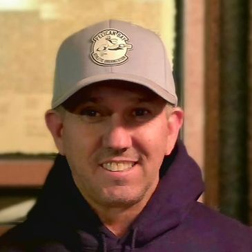 Man smiling wearing a cap and hoodie.