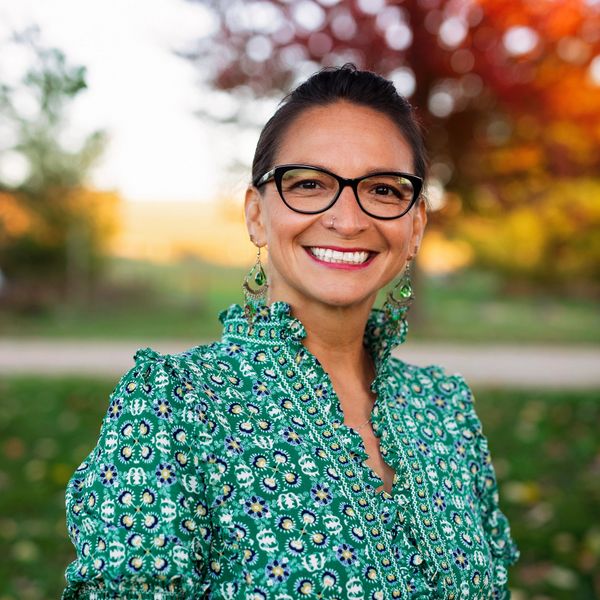 Smiling brown, Mexican woman with green flowery dress wearing black rimmed glasses